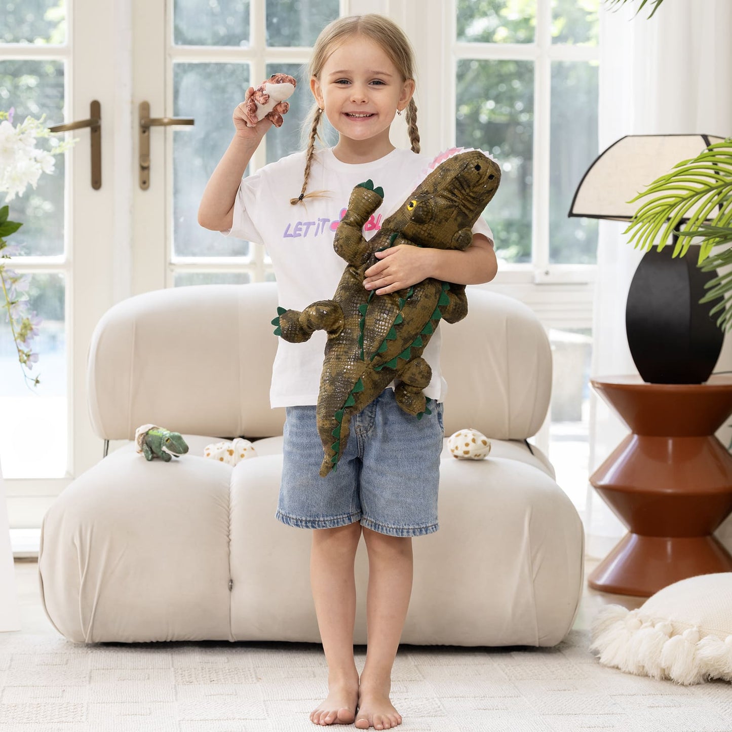 Young girl holding a plush dinosaur toy in a bright living room.
