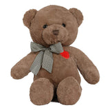 A brown plush teddy bear sitting upright on a white background, wearing a black-and-white gingham bow around its neck and a small red heart patch on the chest.