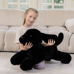 Young girl holding a large black plush dog in a living room.